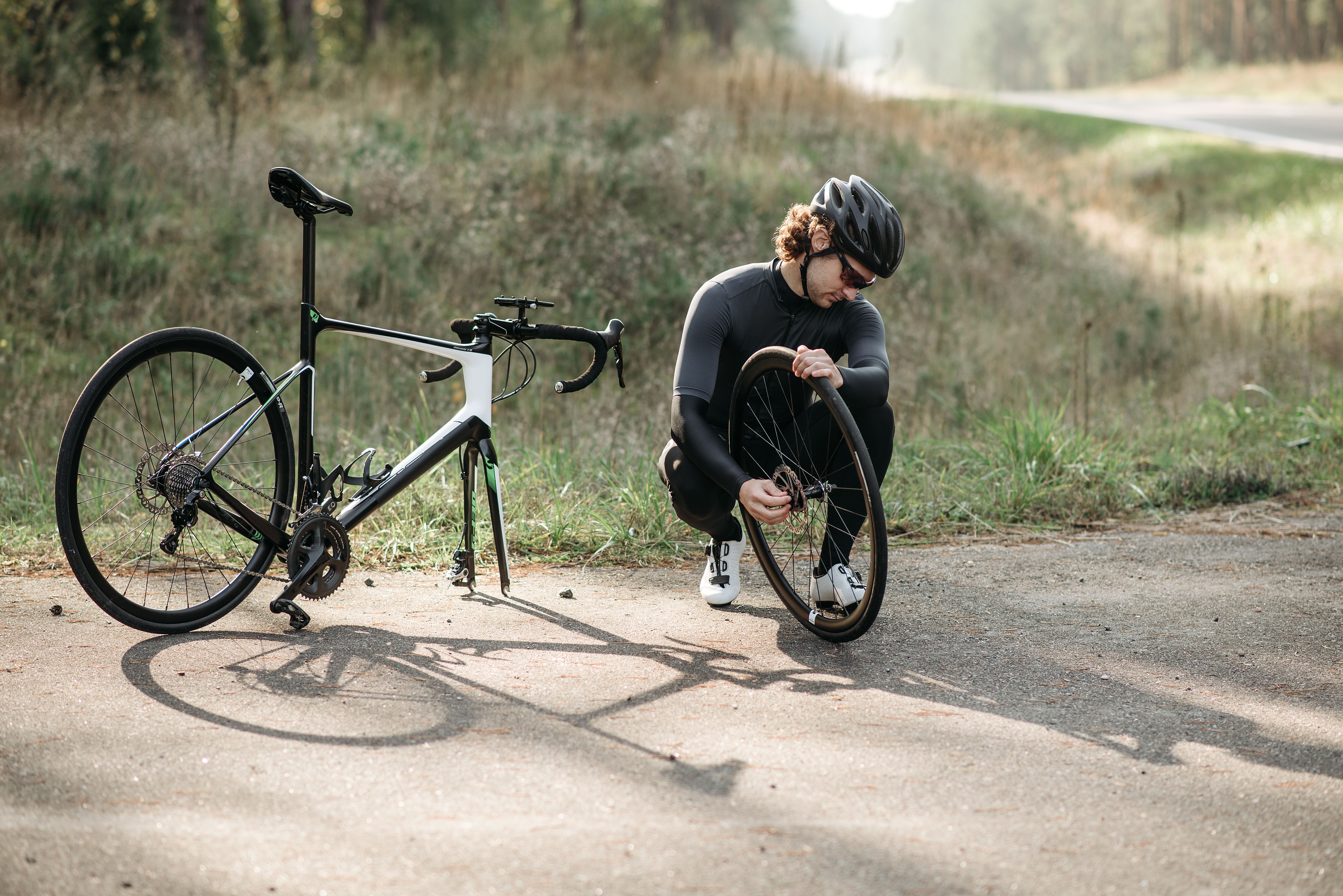 Fietser met helm repareert een lekke band langs een landweg